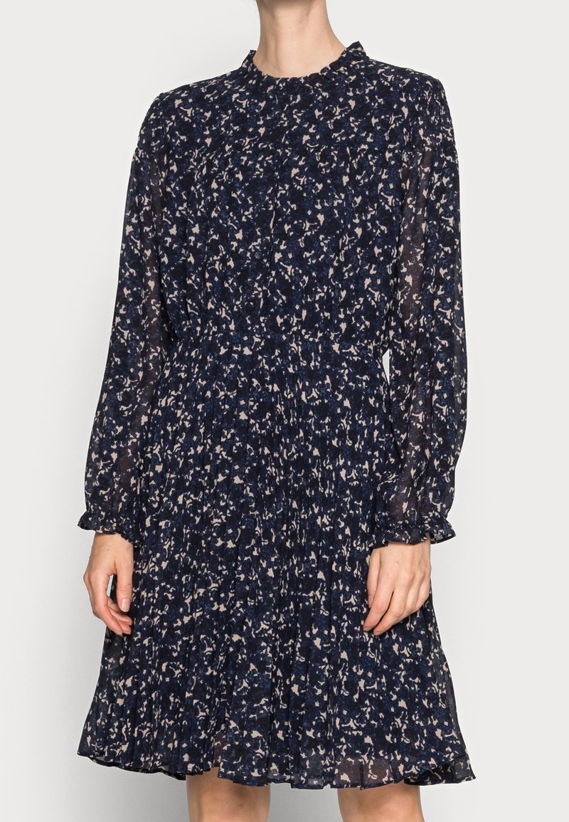 Navy sininen kukallinen mekko pitkillä hihoilla, laskostetulla hameella ja korkealla kaula-aukolla. Valmistettu kevyestä, läpikuultavasta kankaasta, jossa on hienovarainen kuvio.