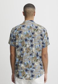 Cămașă cu mânecă scurtă, având o bază bleu deschis, cu un imprimeu tropical de palmieri și flori în nuanțe de bej, verde și albastru.