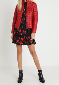 Rød quilted jakke over en sort kjole med blomsterprint. Kjolen har korte ærmer og falder over knæet. Sorte ankelstøvler fuldender looket.