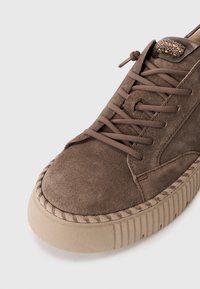 Brune semskede sneakers med rund tå, snøredesign og teksturert såle. Har dekorativt metall på siden.