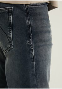 Mörka denimbyxor med rak passform, med en synlig logotagg och subtil slitning, kompletterat av standard bakfickor.