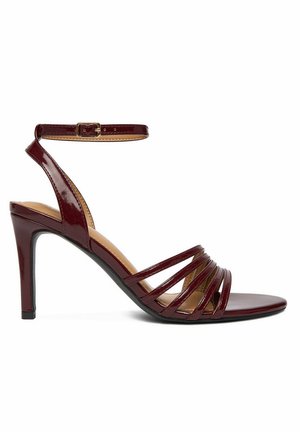 Sandalia de tacón alto en color burdeos con hebilla en el tobillo y múltiples tiras delgadas sobre los dedos, con un acabado brillante.