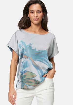 Graphic floral-patterned top in light blue and white stripes, loose fit, boat neckline, short sleeves, paired with white pants.
