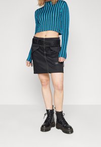 Černá mini sukně s předním zipem a páskem, se širokými kapsami. V kombinaci s cropped svetrem s modro-černými pruhy a černými bojovými botami.