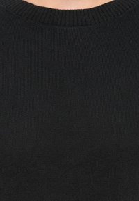 Gros plan sur un torse portant un pull noir à col rond côtelé avec une texture tricotée visible.