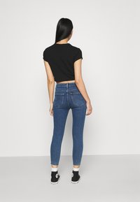 Camiseta negra cortada, ajustada, combinada con unos jeans skinnies de mezclilla azul de talle alto. La textura es suave, con bolsillos traseros elegantes y puños enrollados.
