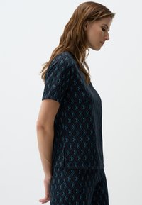 Maglietta a maniche corte di colore scuro con un motivo geometrico in teal su sfondo blu navy, realizzata in un tessuto morbido e liscio con una vestibilità comoda.