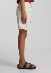 Shorts en denim beige clair avec ourlets repliés, dotés de passants de ceinture et de poches avant, associés à des sandales à plateforme noires et en liège.