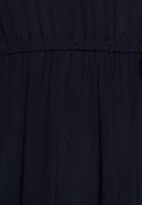 Marineblått tyg med en mjuk textur, med samlad detalj vid midjan och subtila vertikala linjer. Lämplig för avslappnad användning.