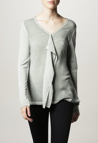 Top lungo a maniche lunghe di un verde chiaro con scollo a V e drappeggio anomalo sul davanti. Tessuto morbido e testurizzato con una leggera lucentezza.