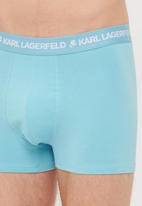Bóxer azul hecho de tela suave, con una cinturilla elástica blanca que lleva el logo "KARL LAGERFELD" y un diseño ajustado.