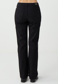 Pantaloni a zampa in denim nero con vita alta, caratterizzati da due tasche posteriori e una texture liscia, rifiniti con una discreta etichetta del marchio in vita.