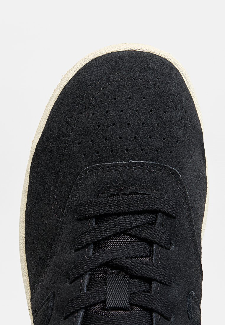 Zwarte suède sneaker met geperforeerde neus, textuur zwarte veters en een crème kleurige rubberen zool. Heeft een minimalistisch ontwerp.