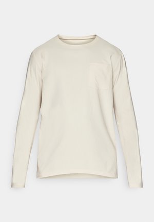 Long-sleeve, crew neck shirt in light beige cotton. Features a subtle pocket on the left chest and curved hem for a relaxed fit.