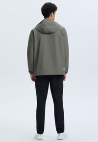 Giacca con cappuccio grigia con polsini elasticizzati, pantaloni neri e sneakers bianche. Design semplice, materiale leggero, branding minimale sull'orlo inferiore.