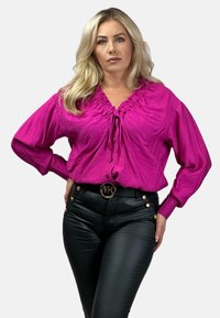 Fuksjowa koszula zapinana na guziki z zebranym dekoltem i długimi rękawami, połączona z czarnymi skórzanymi spodniami o wysokim stanie z złotymi detalami.
