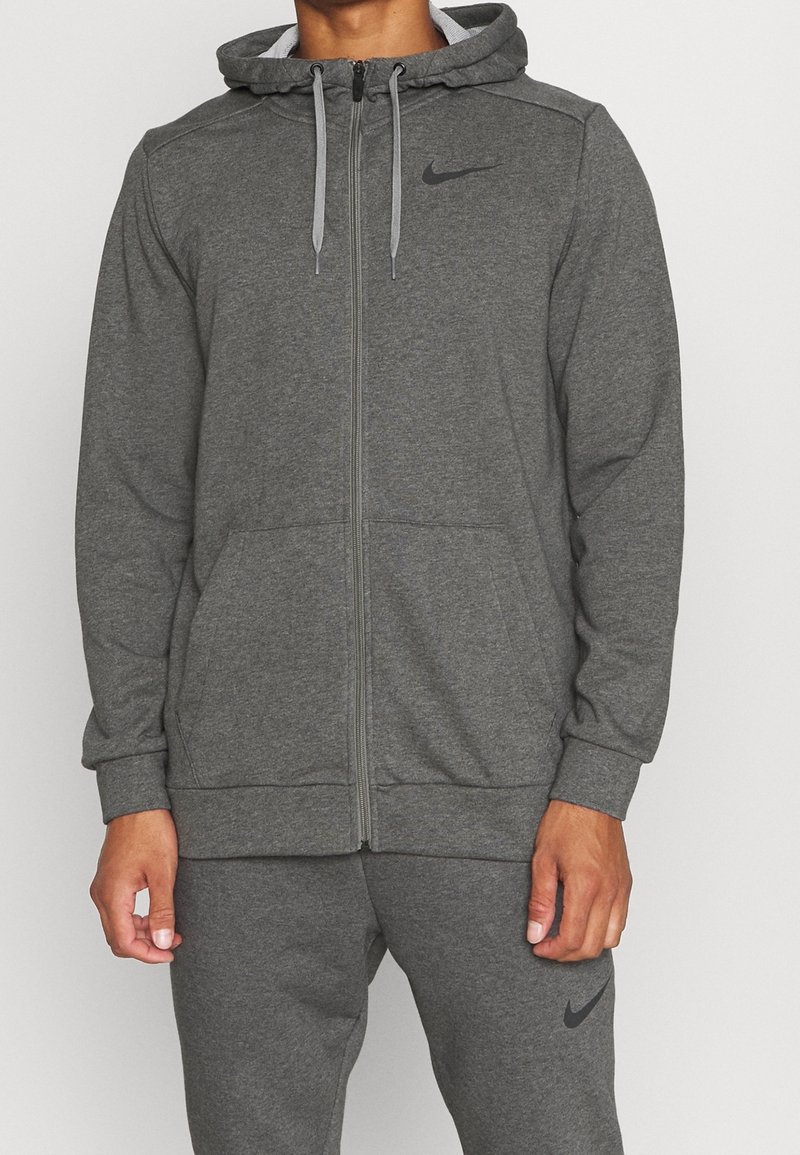 Homme portant un sweat à capuche Nike gris foncé assorti avec poches à l'avant et cordons, ainsi qu'un pantalon de survêtement avec le logo Nike sur la cuisse.