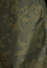 Žalias audinys su subtiliu gėlių raštu, kuriame yra paukščių, lapų ir šviesiai žalių gėlių. Lygus paviršius, sudėtingi dizaino elementai.