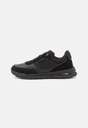 Sneaker nera con una toma in sintetico liscio, dettagli in suede, punta rotonda, chiusura con lacci e suola in gomma texturizzata con dettagli a strisce colorate.