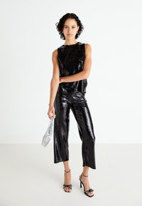 Conjunto de top y pantalones de lentejuelas negras, con un corte holgado. Bolso plateado y tacones negros con acentos de cuentas. Textura suave, superficie reflectante.