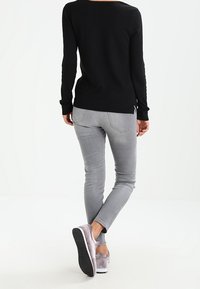 Czarna bluzka z długim rękawem i rozcięciami po bokach, szare dopasowane jeansy oraz szare casualowe buty z teksturowaną gumową podeszwą. Prosty i funkcjonalny design.