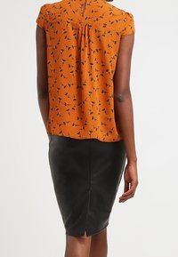 Blusa floreale arancione con maniche corte, abbinata a una gonna a matita in pelle nera con dettaglio dello spacco posteriore.