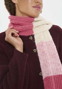 Écharpe en tricot présentant des couleurs dégradées de rose clair, rose foncé et crème. Texture douce avec un motif côtelé, portée avec un cardigan bordeaux.