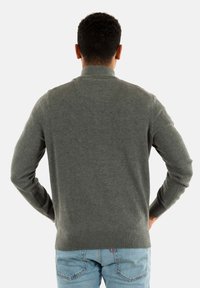 Maglione grigio a maglia con colletto alto, maniche lunghe e polsini a costine. Indossato sopra jeans azzurri chiari, che mostrano un design semplice e senza soluzione di continuità.