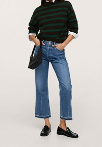 Pull rayé vert et marron, jean bleu taille haute avec ourlets effilochés, et mocassins noirs. Un petit sac à main noir complète le look.