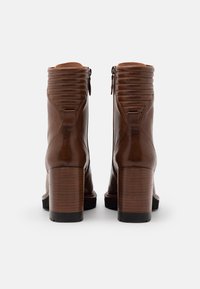 Bottines en cuir marron avec un talon empilé, des détails côtelés en haut et des fermetures éclair sur le côté. Texture lisse avec une finition brillante.