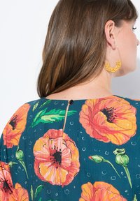 Blomsterkjole med store orange valmueprint på en mørkegrøn baggrund, med en nøglehulslukning og en sort knapdetalje på ryggen.