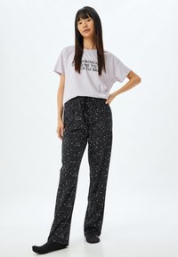 Paarse t-shirt met korte mouwen met zwarte tekst, gecombineerd met zwarte pyjamabroek met een wit hemellichaampatroon en een elastische tailleband.