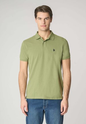 Polo shirt verde oliva chiaro con colletto, maniche corte e un piccolo logo blu navy sul lato sinistro del petto. Abbinato a jeans blu.