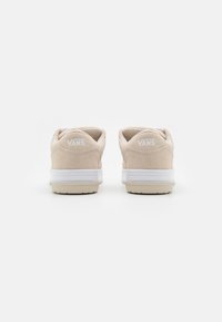 Beige mockalädersneakers från Vans med vita accenter, med en låg profil och gummisulor, sedd bakifrån.