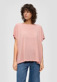 Top lavorato a maglia di un rosa chiaro con vestibilità ampia, dotato di maniche corte e un motivo a rete testurizzato sul davanti. Abbinato a jeans blu.