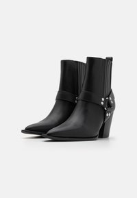 Botines de cuero negro con punteras puntiagudas, detalles acanalados y una correa decorativa con herrajes plateados. Los tacones cuadrados ofrecen estabilidad.