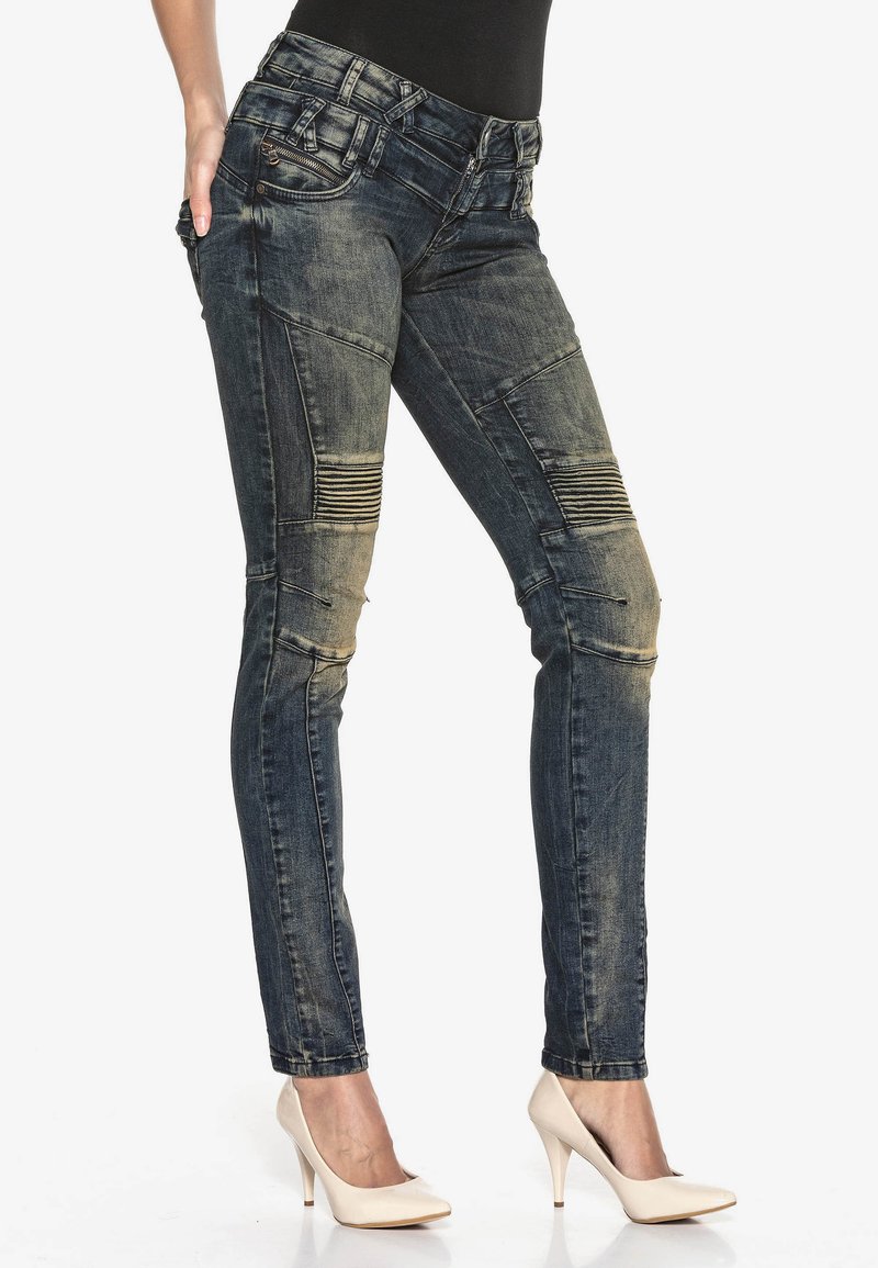 Engen Jeans aus dunklem Denim mit distressed Finish, ausgestattet mit gerippten Stoffakzenten an den Knien und Reißverschlusstaschen.