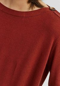 Maglione rosso lavorato a maglia con scollo a barca, tessuto testurizzato e dettaglio con bottone sulla spalla per un tocco di design in più.