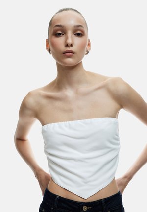 Wit strapless top met een geraffineerde textuur en een puntige zoom. Gepaarde met donkerdenim jeans, met minimale details en een gladde stofafwerking.