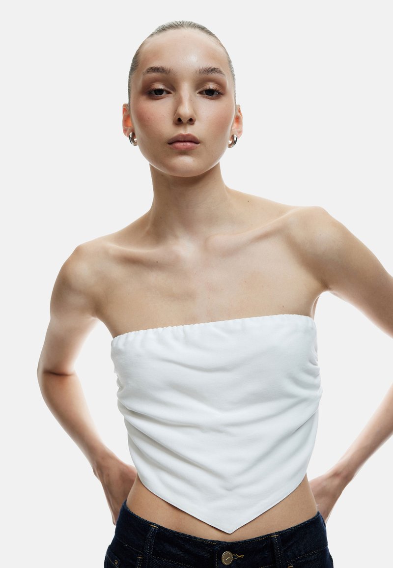 Wit strapless top met een geraffineerde textuur en een puntige zoom. Gepaarde met donkerdenim jeans, met minimale details en een gladde stofafwerking.