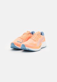 Zapatillas de correr ligeras en color melocotón con acentos en azul. Parte superior de malla con acabado texturizado, diseño de cordones y suela de goma con patrón.