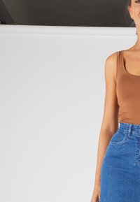 Débardeur marron ajusté associé à une jupe en denim bleu taille haute. Texture lisse, design simple et détails de couture classiques visibles.