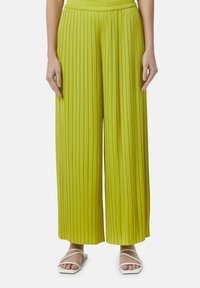 Limoengroene, geplooide wijde broek met een elastische tailleband, gecombineerd met witte sandaaltjes met bandjes.