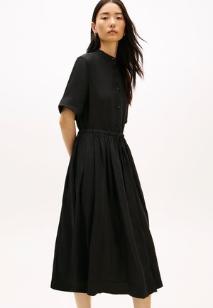 Melna kreklveida kleita no viegla auduma, ar īsām sarullētām piedurknēm, elastīgu jostasvietu un pilnu, plūstošu svārku.