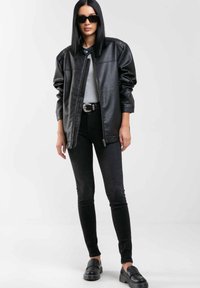Črna usnjena oversize jakna z zadrgo in zloženim ovratnikom, v kombinaciji s črnimi skinny hlačami in črnimi natikači.