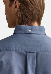Džinsu krekls ar apkakles izgriezumu, aizmugurējo plecu daļu un vienu pogu pie apkakles. Mīksta tekstūra vidēji zilā tonī.