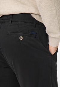 Pantaloni neri in tessuto morbido, con una tasca posteriore con chiusura a bottone e una piccola etichetta con il marchio. Design casual con una vestibilità aderente.