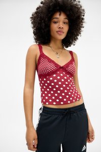 Red polka dot camisole with lace trim and adjustable straps, paired with black joggers featuring white stripes along the sides.