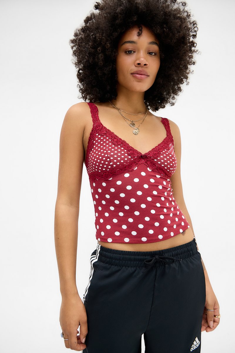 Red polka dot camisole with lace trim and adjustable straps, paired with black joggers featuring white stripes along the sides.