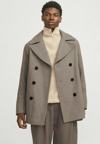 Manteau en laine marron avec un large col, design crois�é, six boutons noirs, et coupe décontractée, porté sur un pull en tricot beige clair.